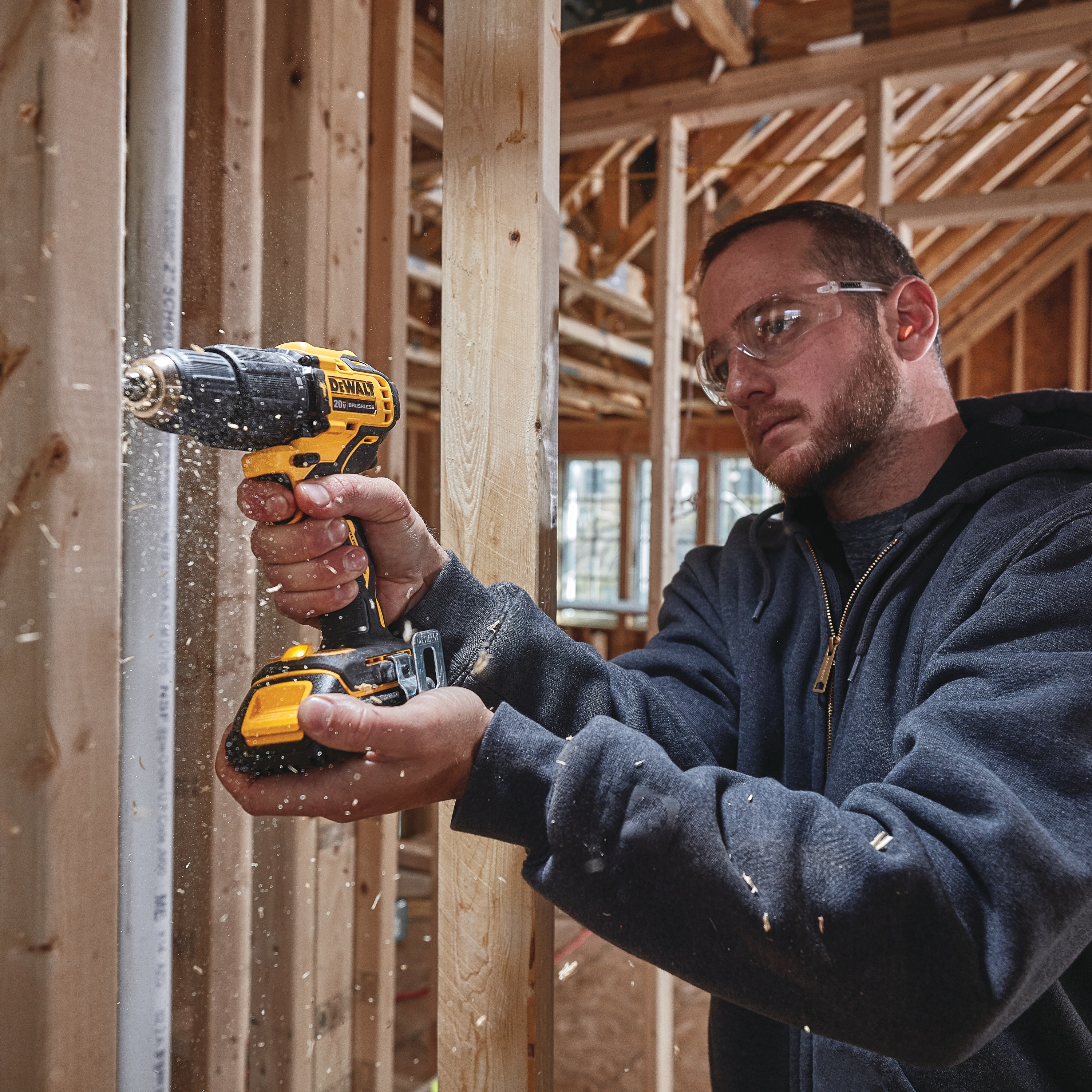 Atomic cordless compact half inch hammer drill driver is being used by a person to drill  wooden plank.