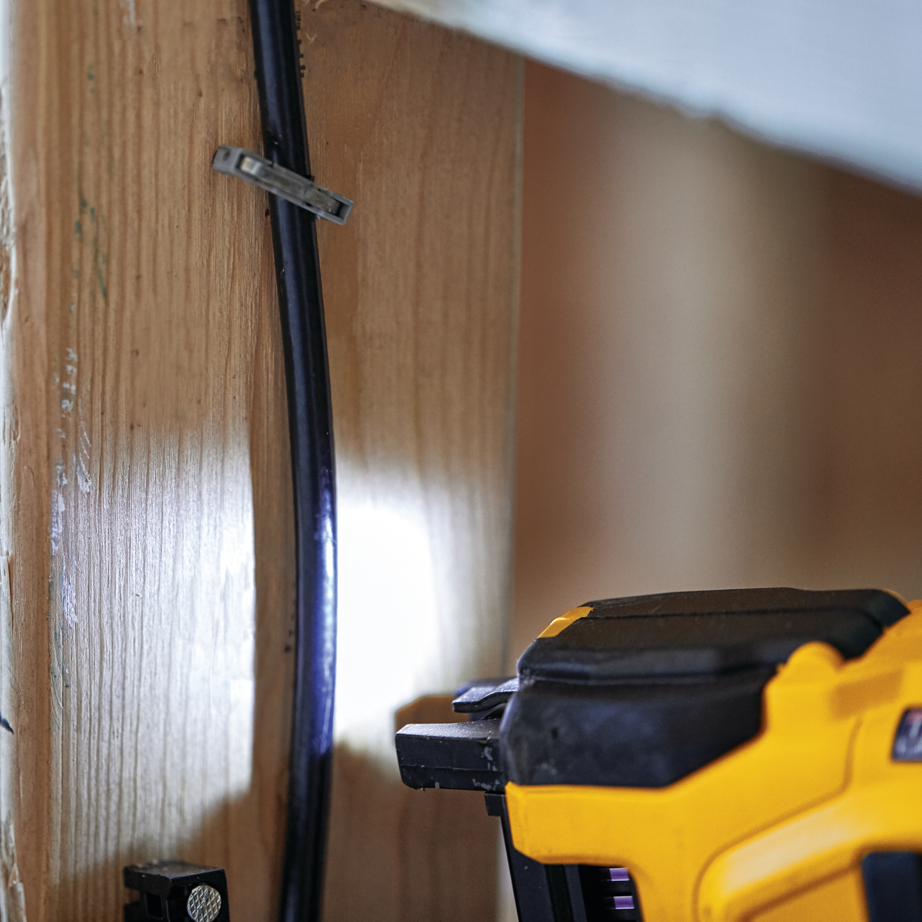 close up of beam light feature of a Cordless Cable Stapler lighting up area of action on wooden wall