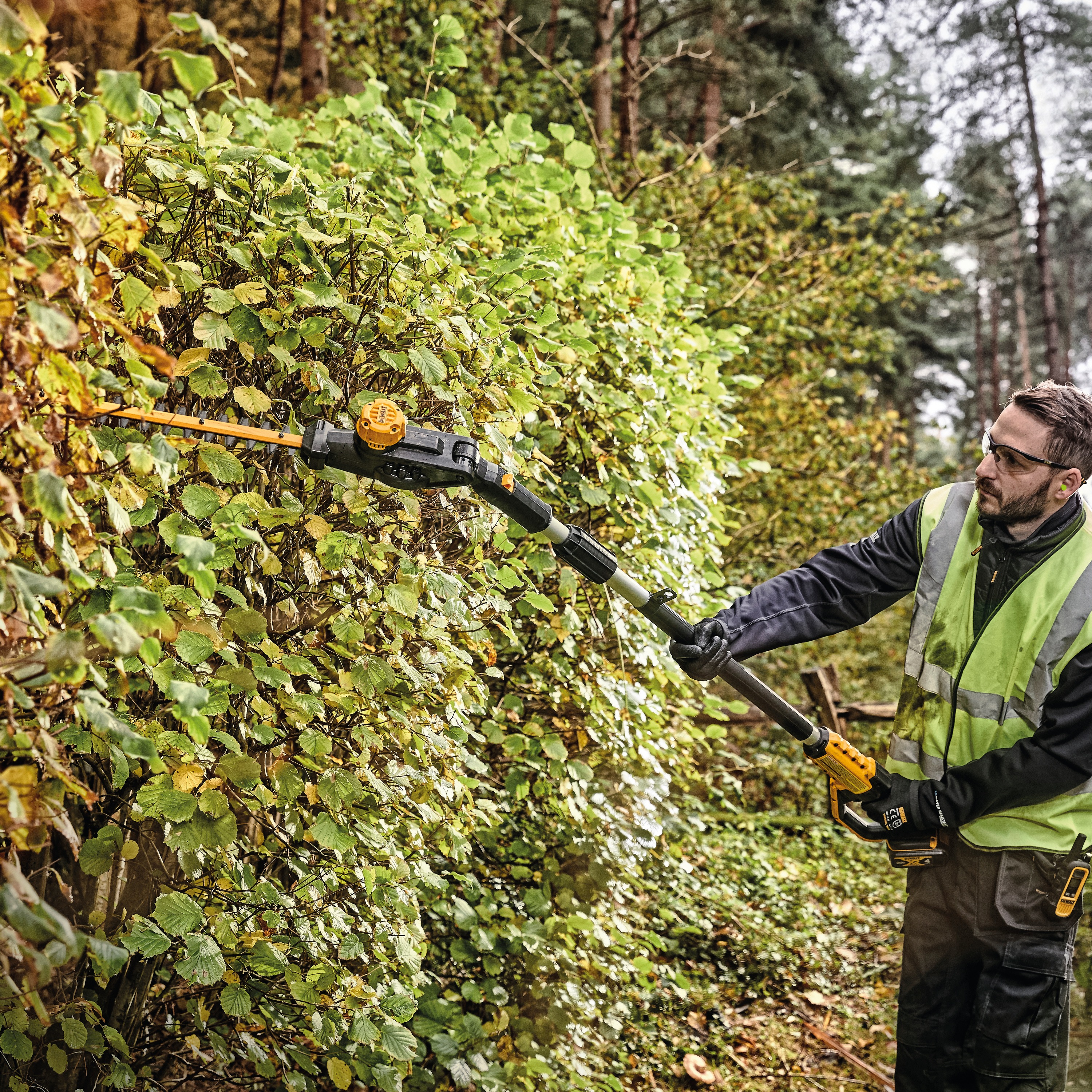 Pole Hedge Trimmer being used by a person to cut through landscape outgrowth.