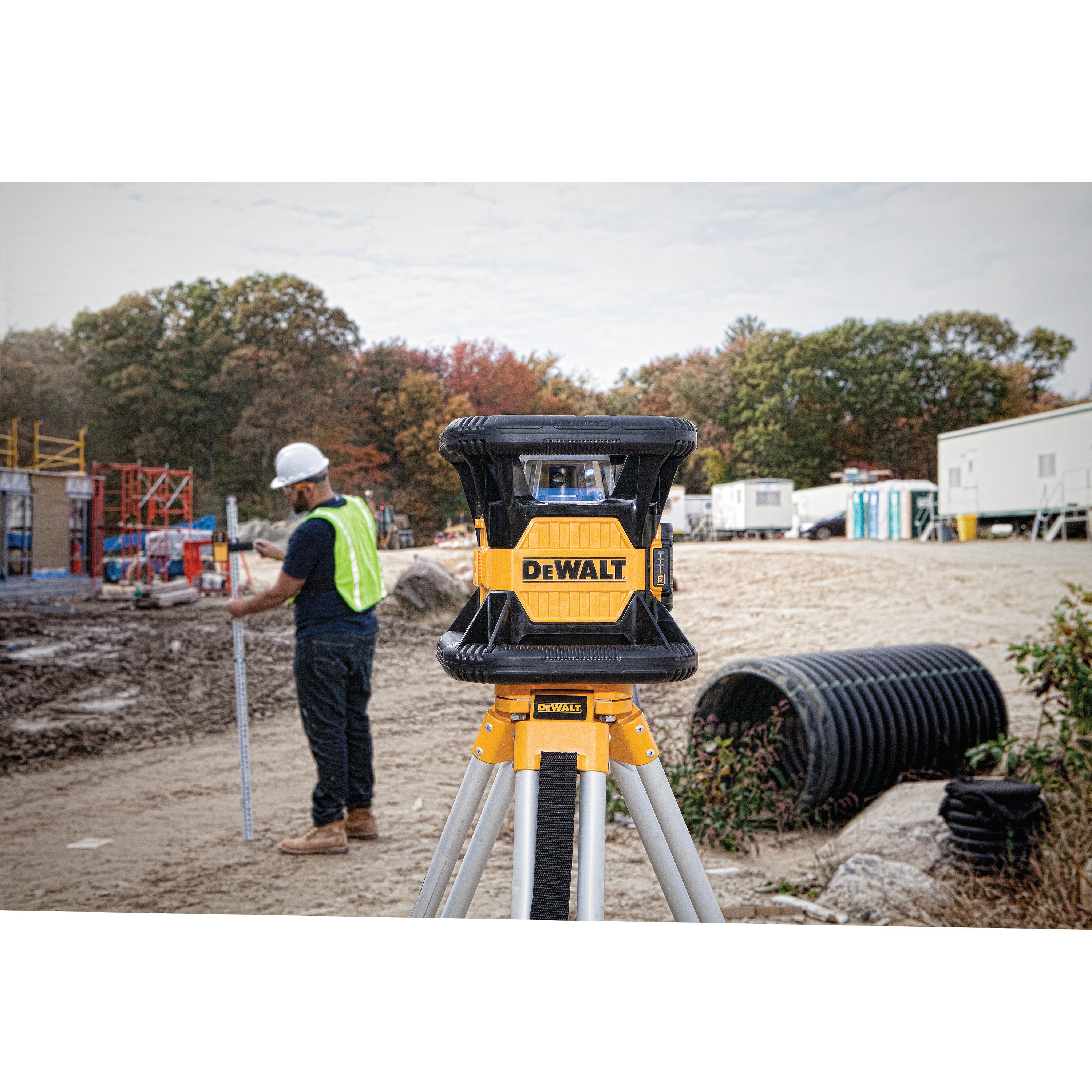 Red rotary tough laser mounted on a tripod being used at a construction site.