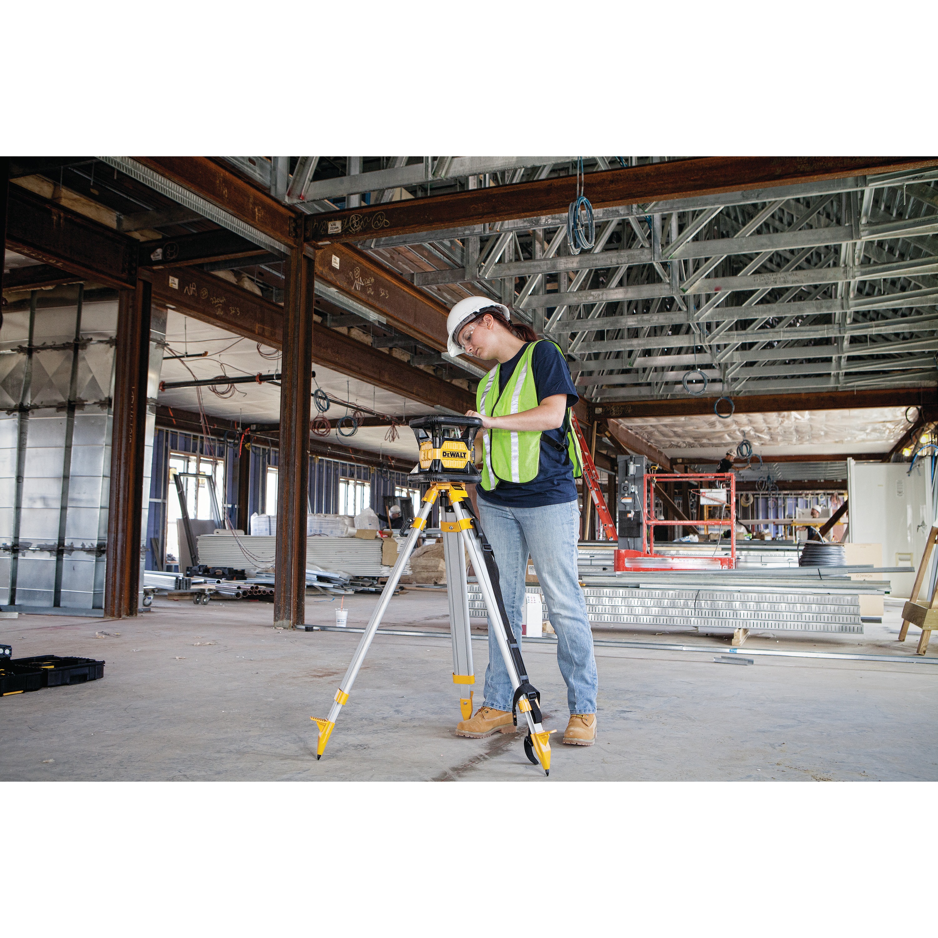 Red rotary tough laser mounted on a tripod being used by a construction worker.