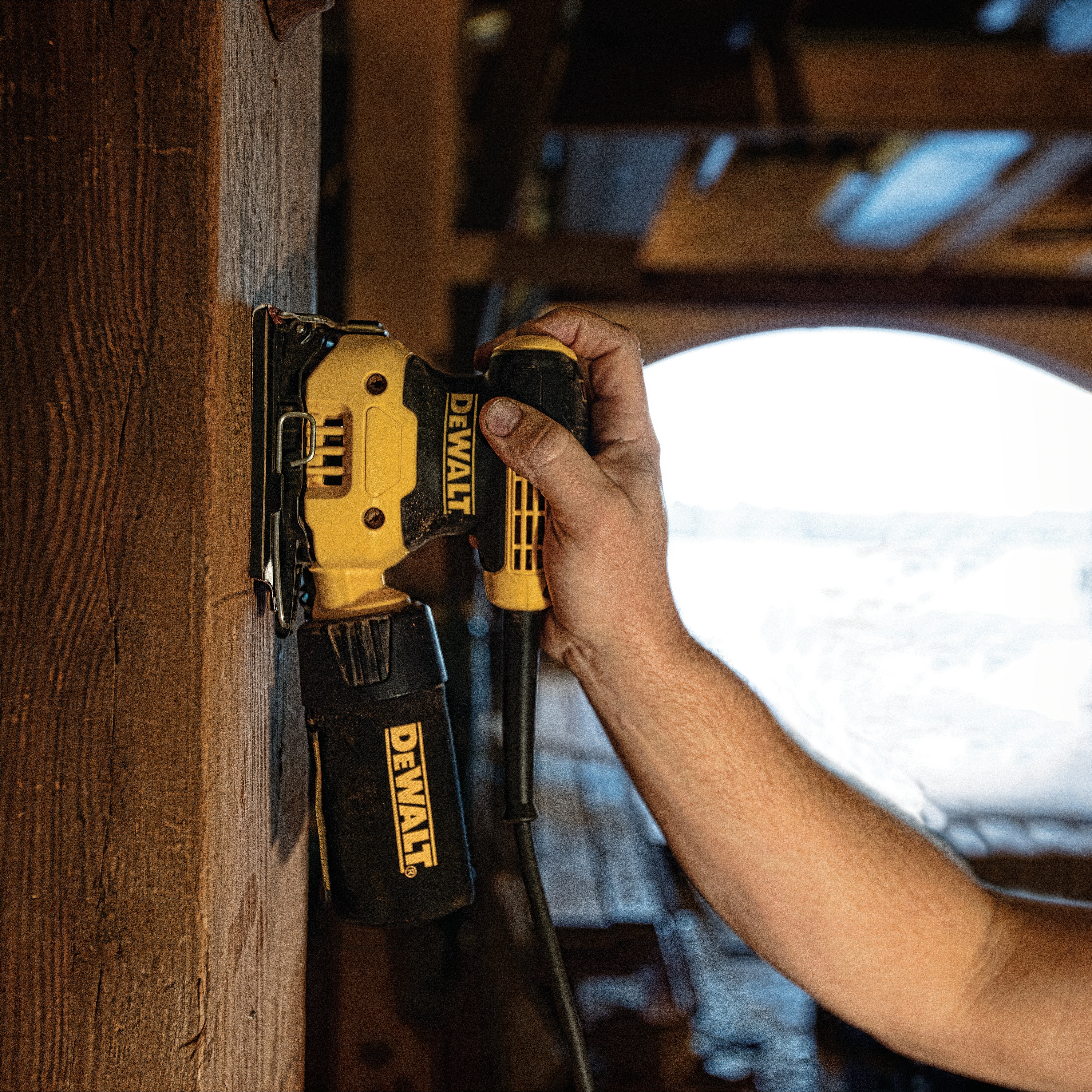 One quarter inch sheet palm grip sander sanding on a wooden wall at a worksite.