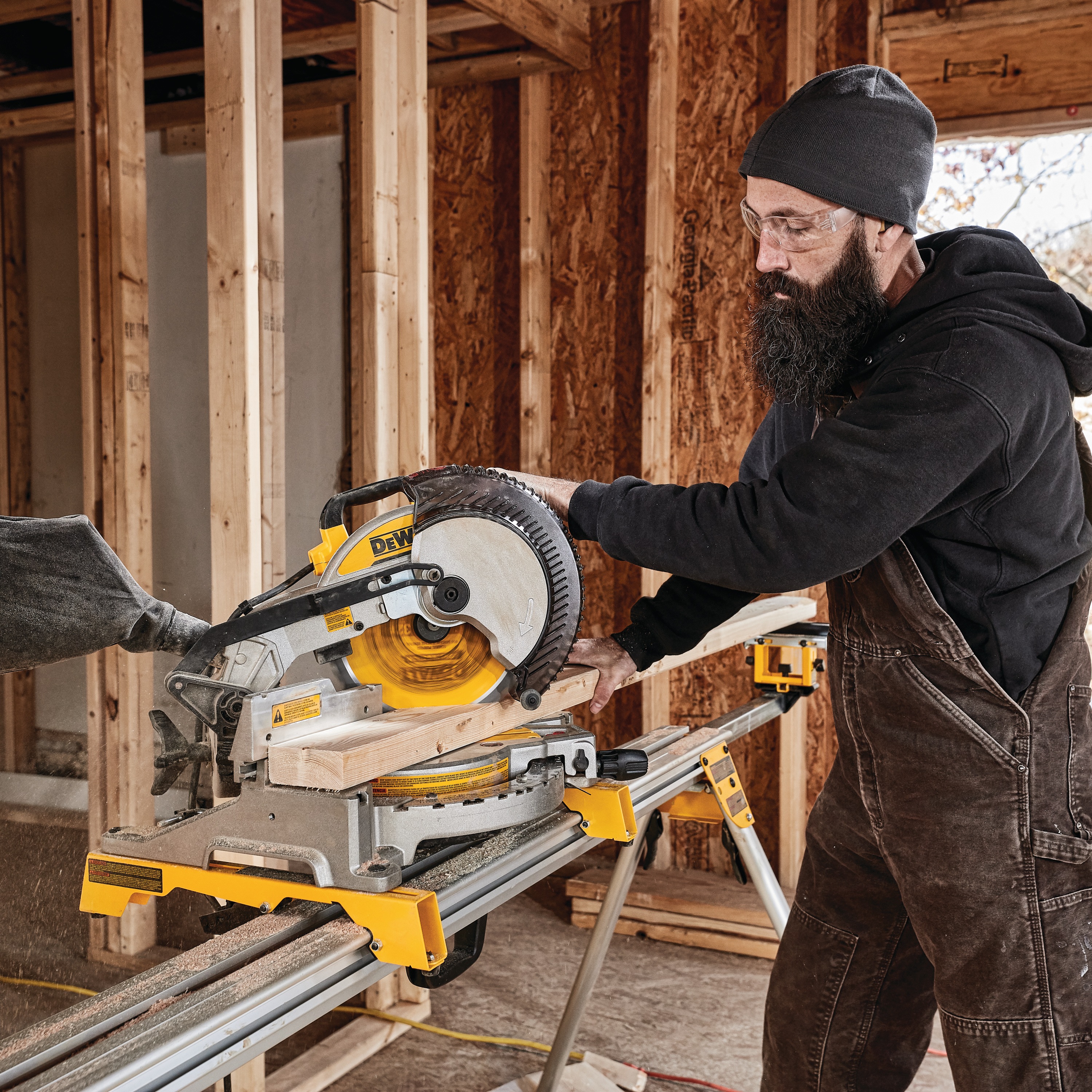 Electric single bevel compound miter saw being used by a person to cut wood.