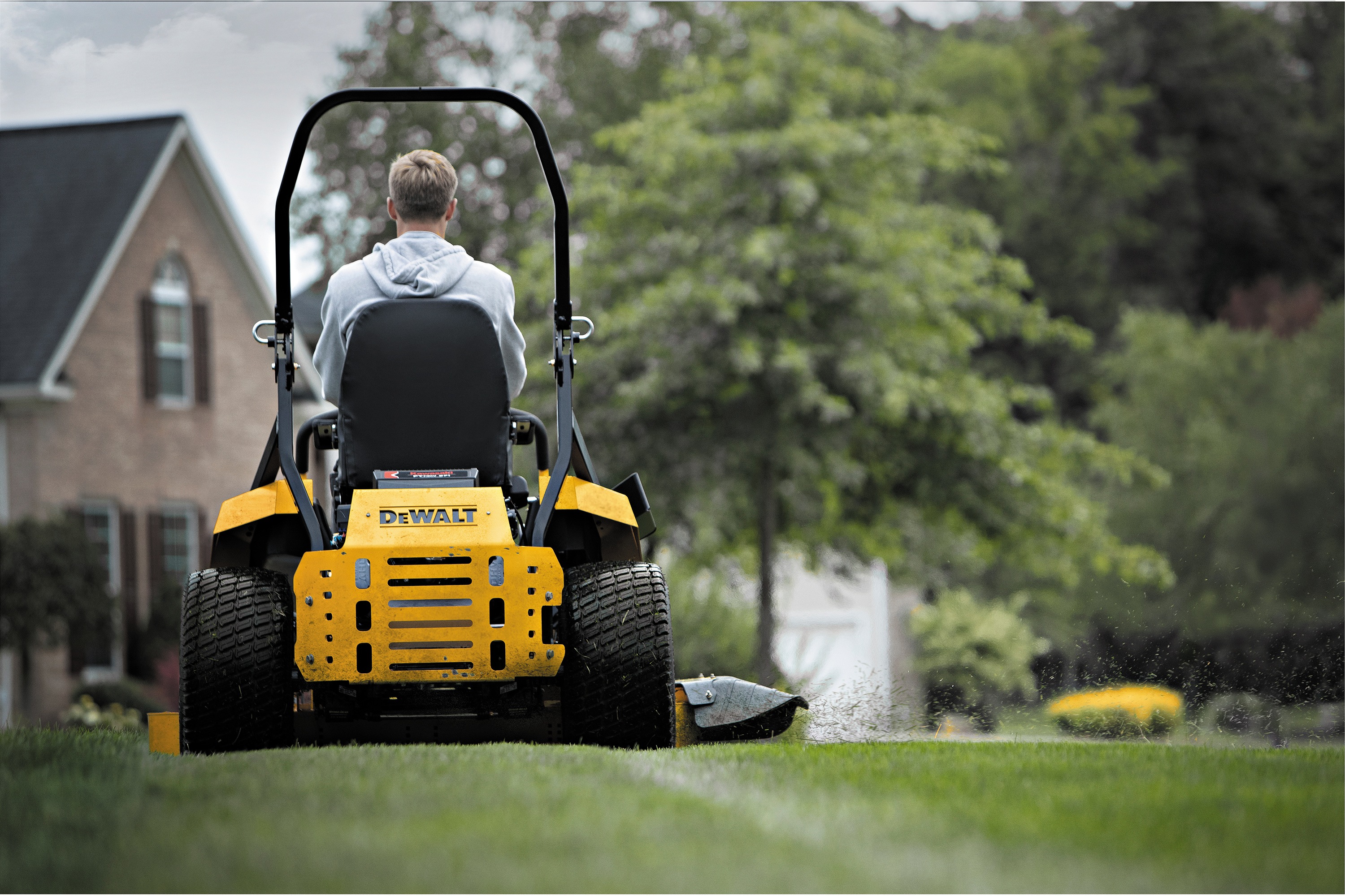 Backside view of 54 inch Kawasaki Gas Hydrostatic Commercial Zero Turn Mower being used by person to mow lawn. 