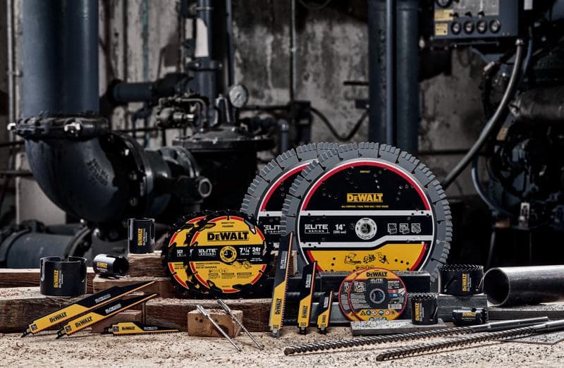 A selection of DEWALT industrial cutting and drilling tools, including saw blades, reciprocating saw blades, drill bits, and abrasive wheels, displayed on a workbench with industrial machinery in the background.
