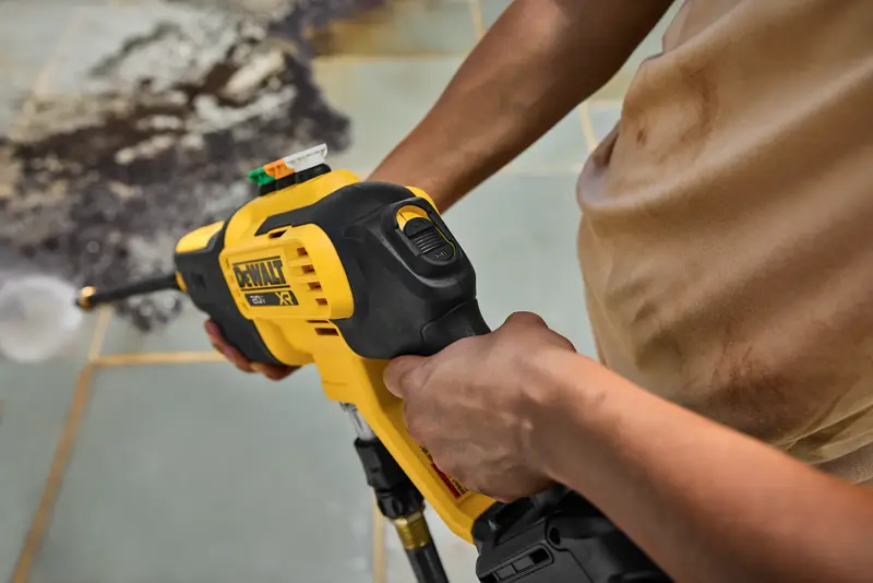 Person using a DEWALT DCPW700B power washer to clean a dirty tiled outdoor surface.