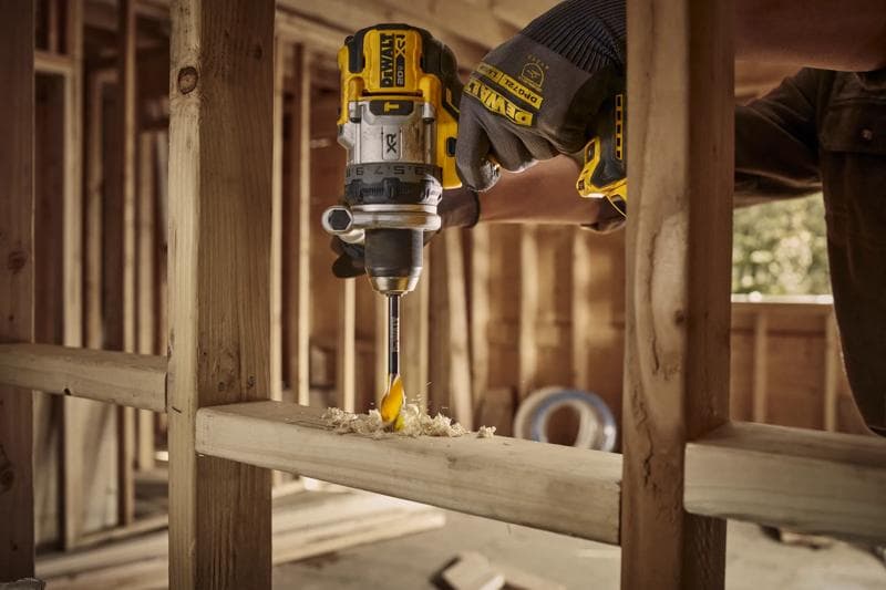 A DEWALT cordless drill is being used by a person wearing gloves to drill a hole into a wooden beam at a construction site.