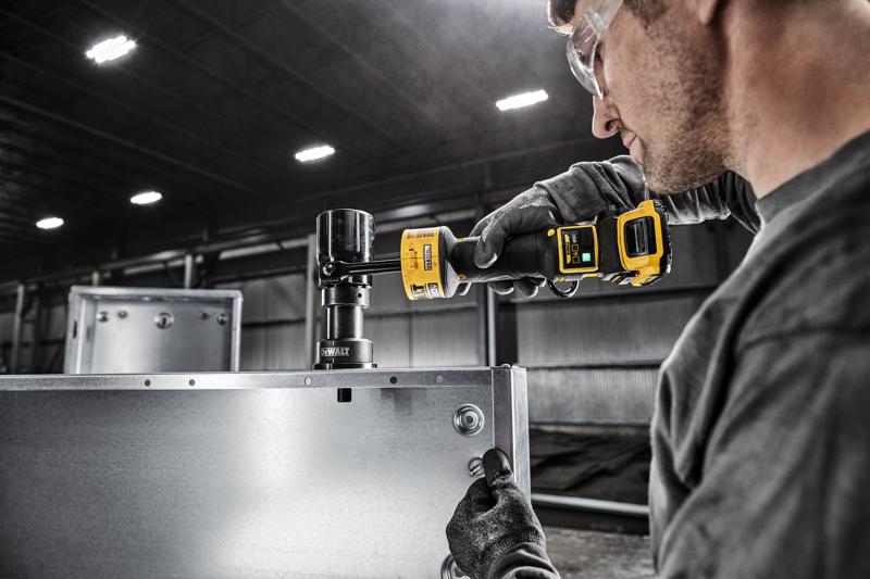 A person is using a DEWALT power tool to make a circular cut in a metal panel inside an industrial setting. The person is wearing gloves to handle the equipment safely. The image focuses on the tool and work area, with the individual's face blurred for privacy.