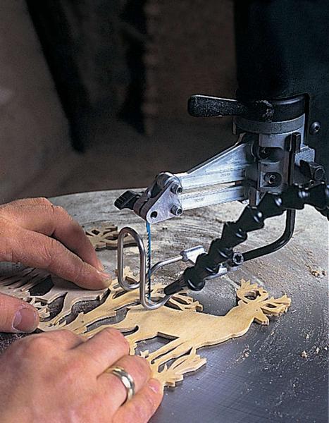 Close-up of hands guiding a piece of wood on a scroll saw, with sawdust visible on the table.