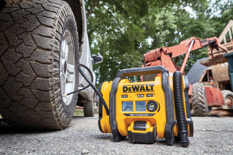 A DEWALT portable air inflator (model DCC020IB) is shown in use, inflating a vehicle tire outdoors. Construction equipment and a tree-filled background are visible.