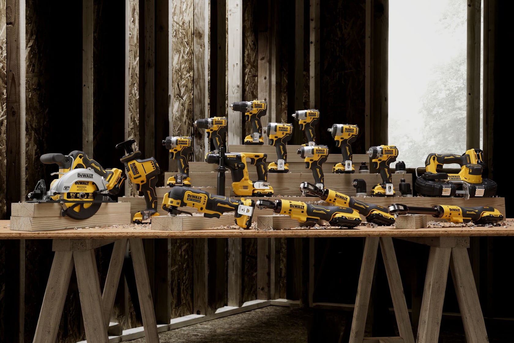 A collection of yellow and black DEWALT power tools displayed on wooden tables inside a construction area with unfinished walls.