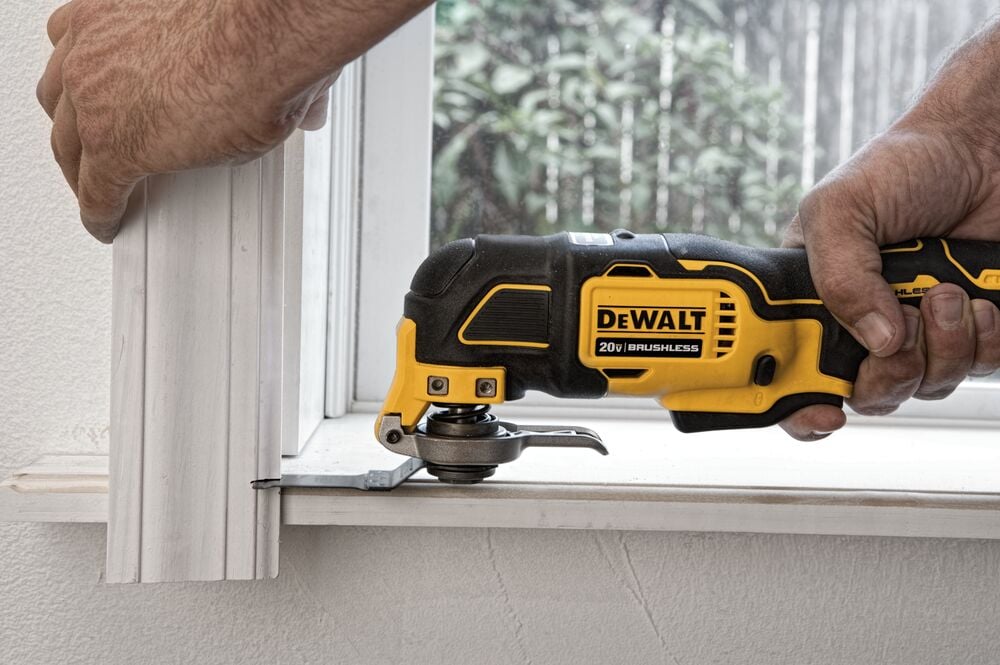 A person uses a DEWALT 20V brushless oscillating multi-tool to cut through a piece of trim or molding near a window.