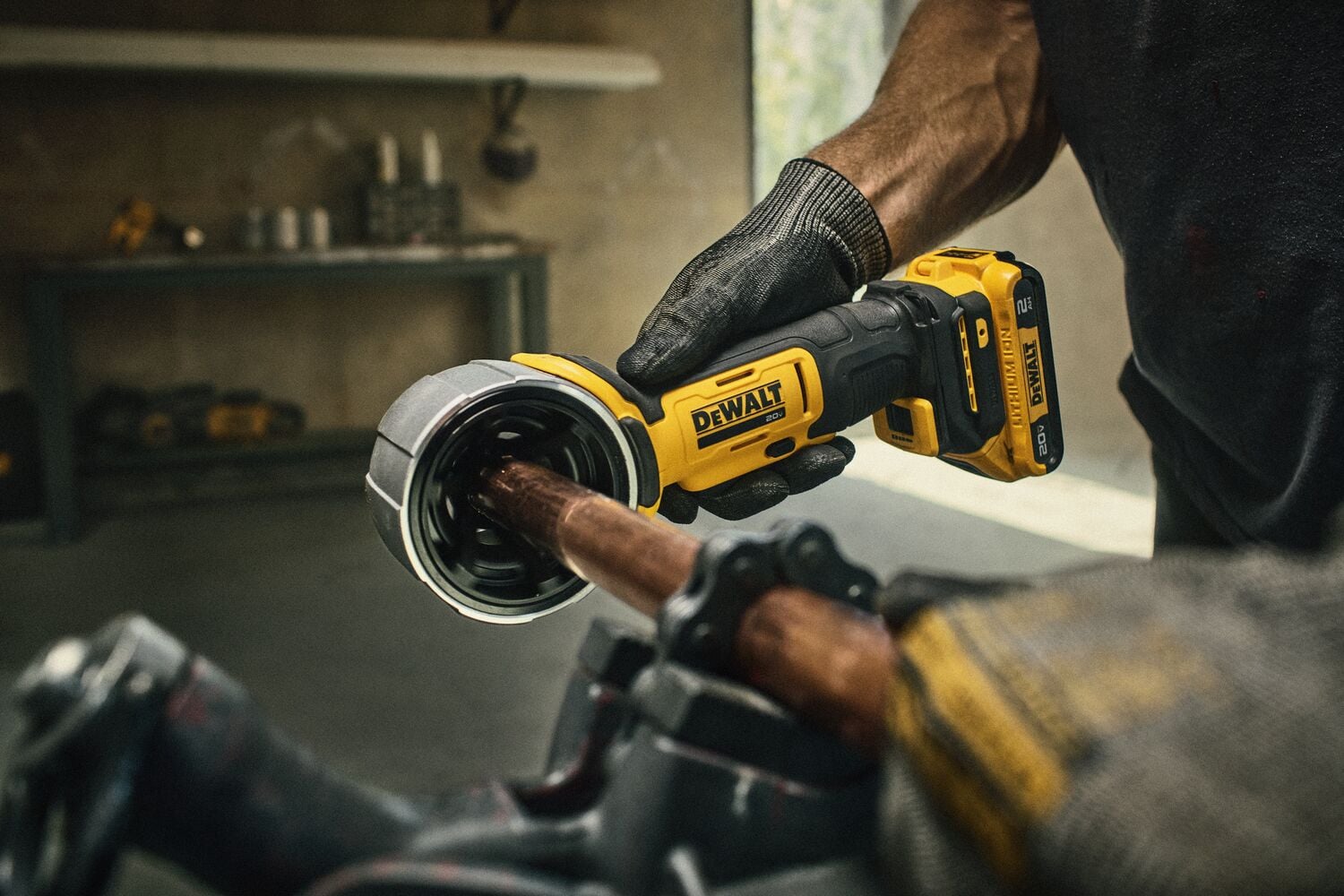 A person wearing gloves uses a DEWALT battery-powered pipe cutting tool to cut a copper pipe in a workshop setting.