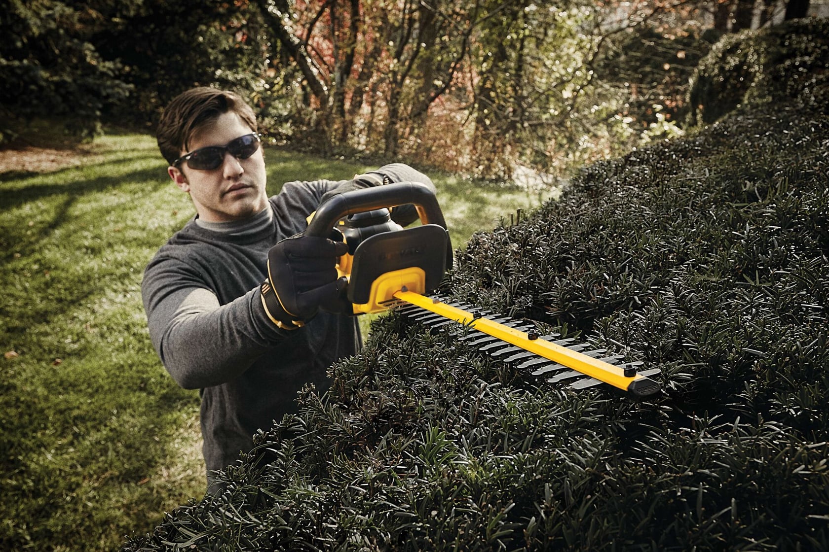 Lithium ion hedge trimmer being used by a person to mend hedge