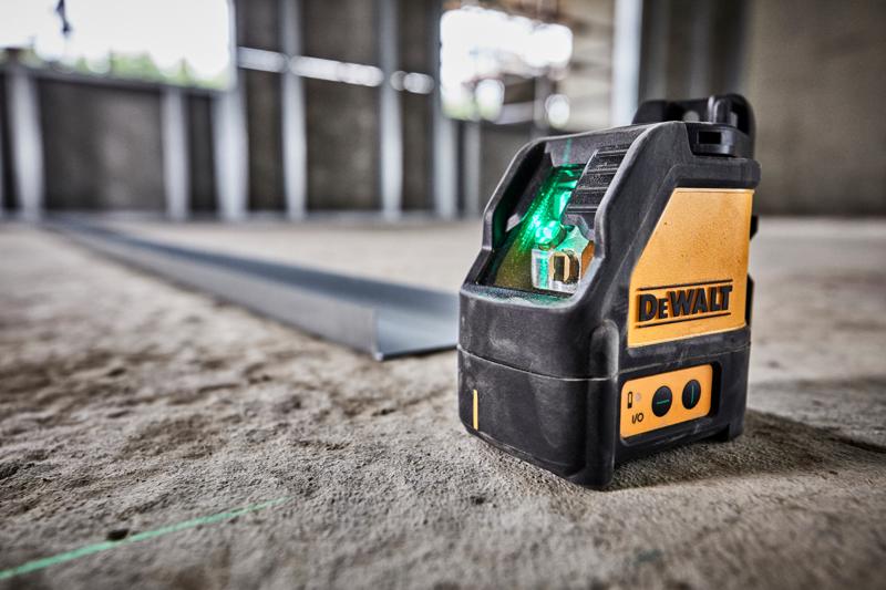 A DEWALT DW088CG green laser level placed on a concrete floor in a construction site, projecting a green laser line for alignment.