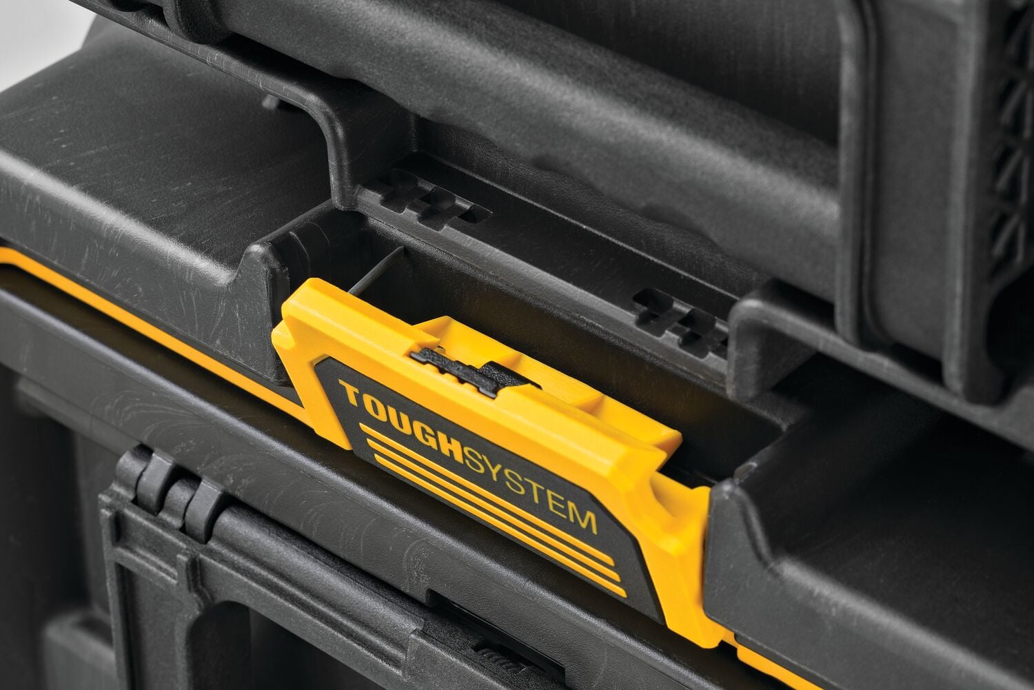 Close-up of a DEWALT ToughSystem locking mechanism on a black and yellow tool storage box. The image shows the interlocking system used to securely stack and connect multiple storage units.