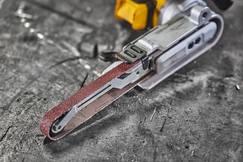 Close-up of a DEWALT electric belt sander on a scratched metal surface.