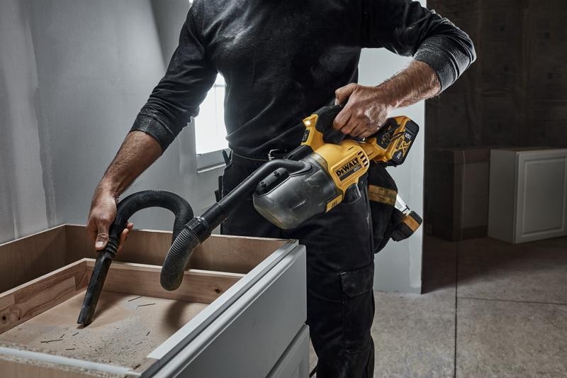 DEWALT 20 MAX* Hand Vacuum vacuuming with flexible tube and crevice tool vacuuming up debris from a home remodeling job site cabinet. DEWALT 5AH battery is being used.