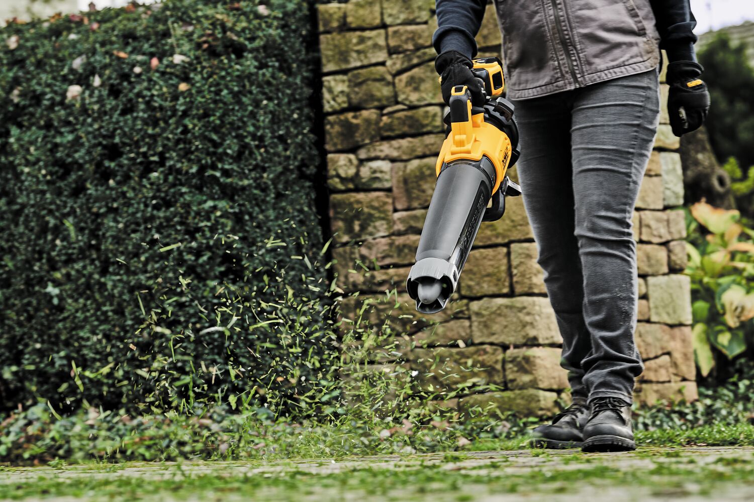 LITHIUM ION XR® Brushless, handheld blower with nozzle being used by a person to blow grass blades off  ground. 