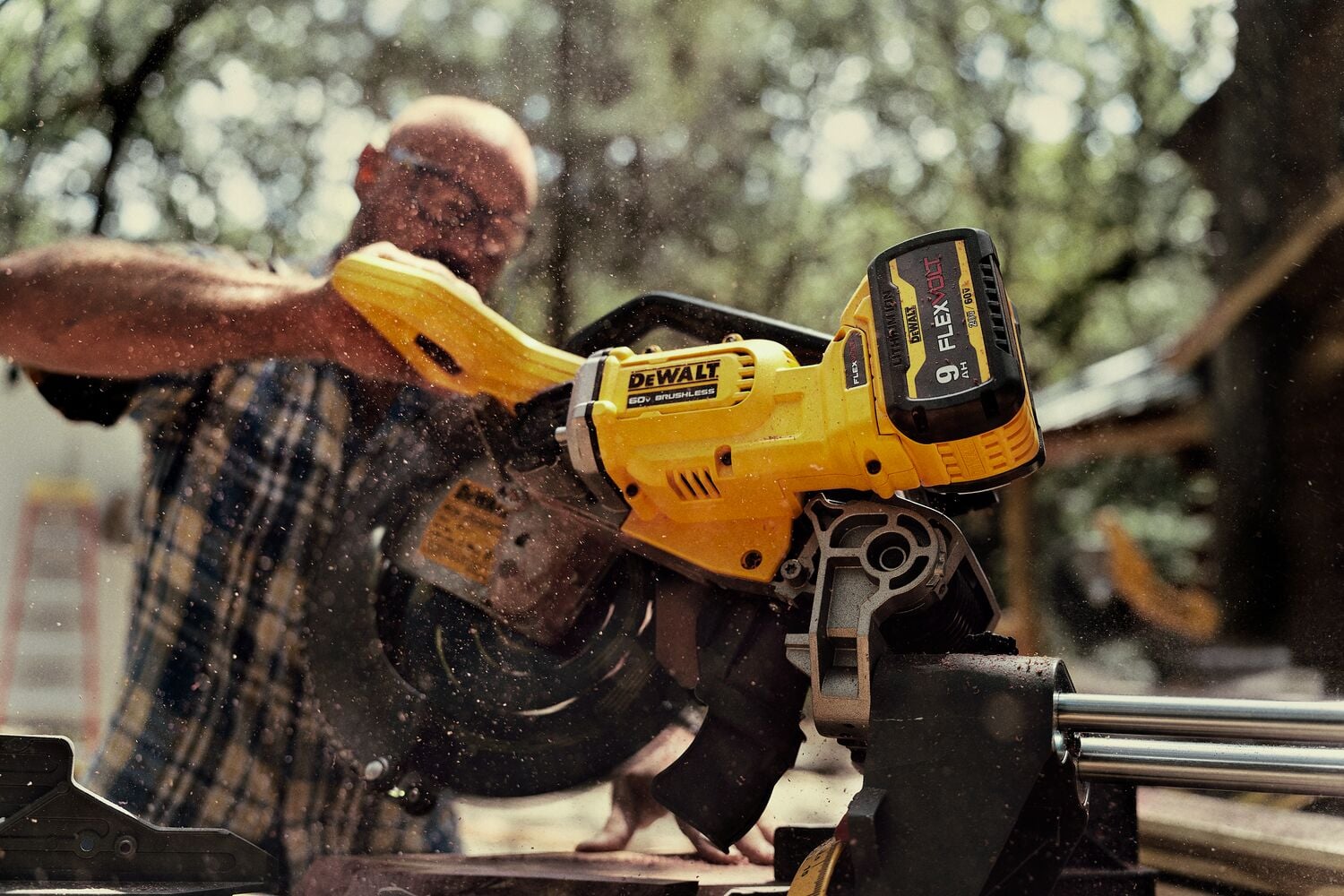 A person using a DEWALT cordless miter saw outdoors, creating sawdust while cutting wood.