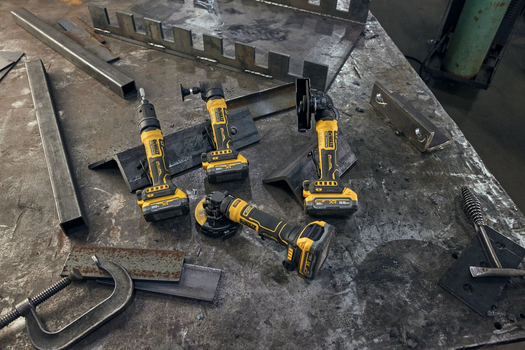 Three DEWALT cordless power tools are placed on a metal workbench surrounded by various metal parts and industrial equipment.