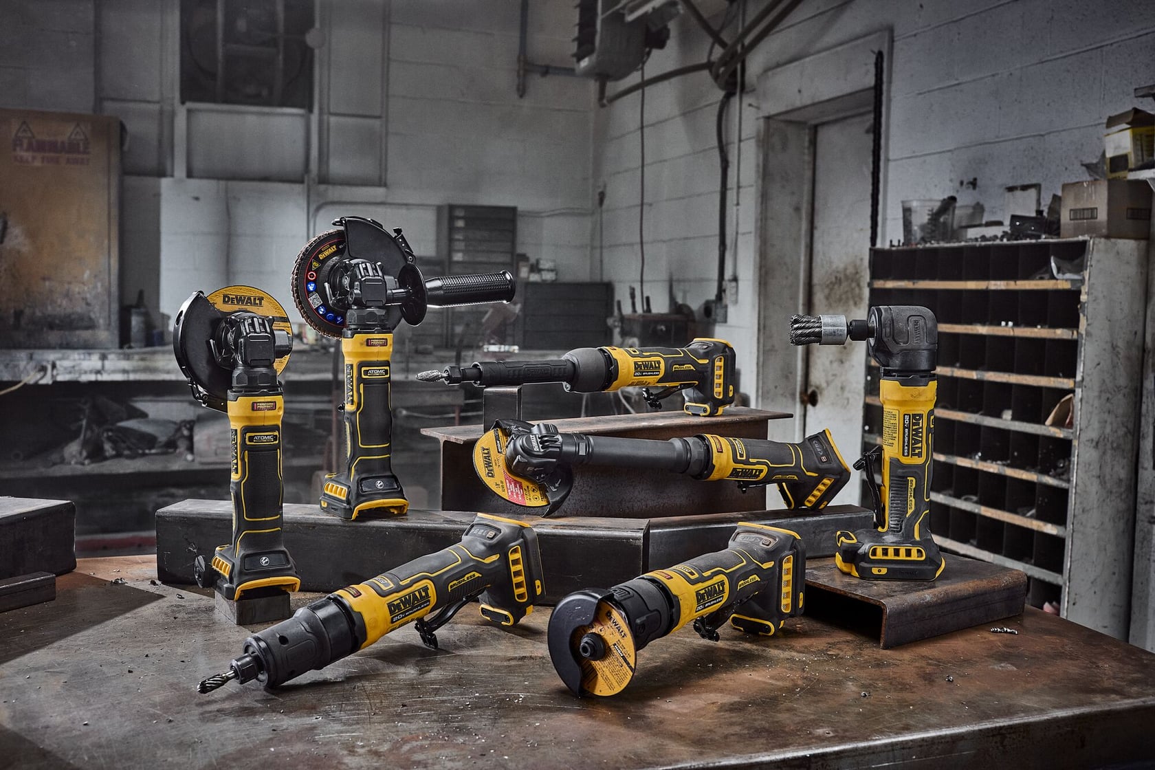 A group of DEWALT cordless power tools, including grinders and rotary tools, are displayed on a workbench in an industrial workshop setting.