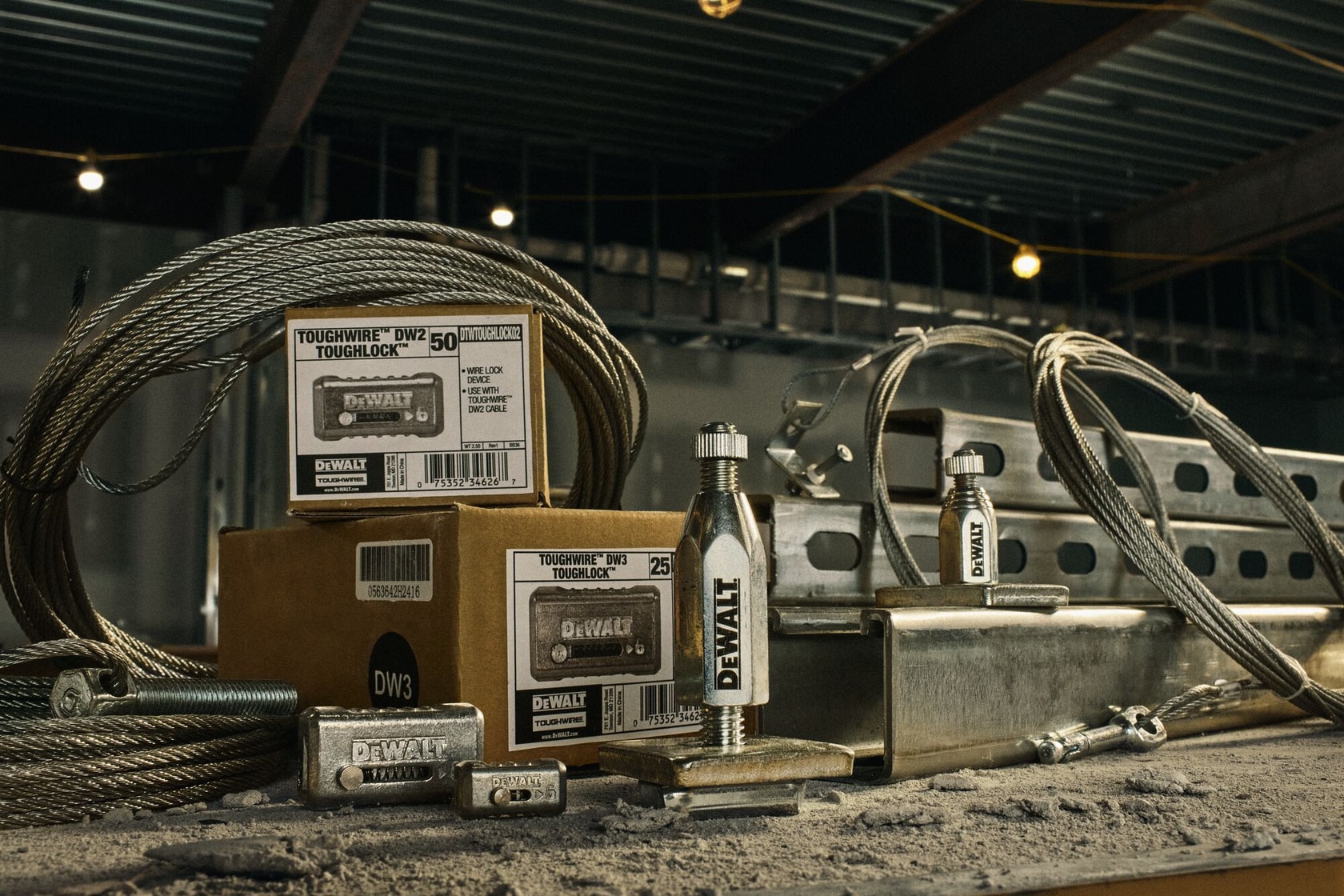A display of DEWALT Toughwire DW2 and DW3 Toughlock cable locks and accessories, including boxed products, metal cable wire coils, and locking devices on a dusty workbench in an industrial setting.