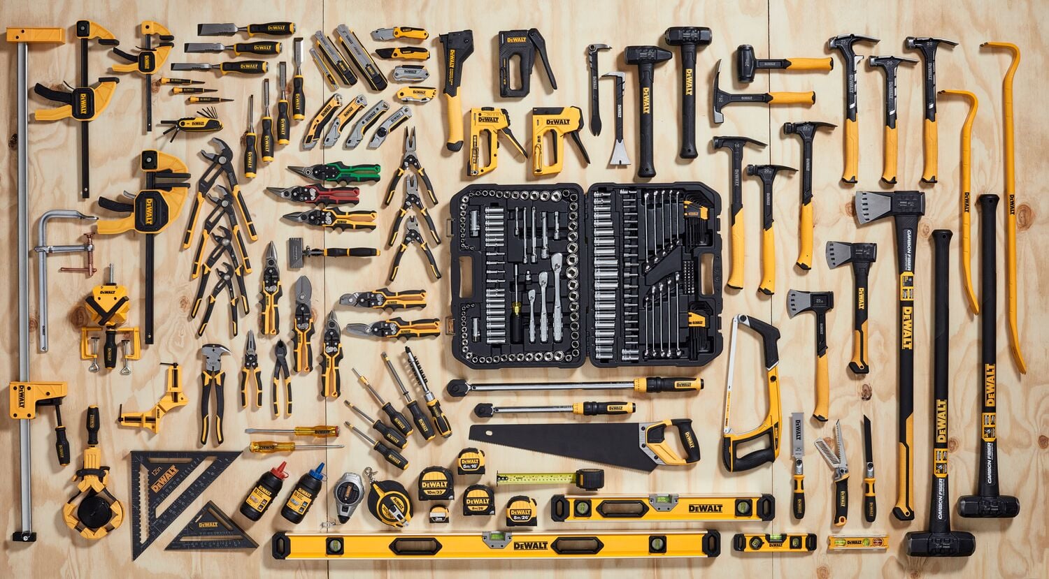 A wide assortment of DEWALT hand tools and measuring instruments neatly arranged on a wooden surface. This collection includes hammers, pliers, screwdrivers, wrenches, tape measures, clamps, levels, saws, and a toolkit with sockets and ratchets, all in yellow and black colors.